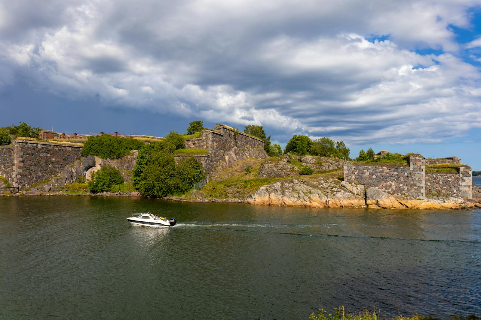 A scenic view of Suomenlinna Fortress with a boat passing by on a sunny day.