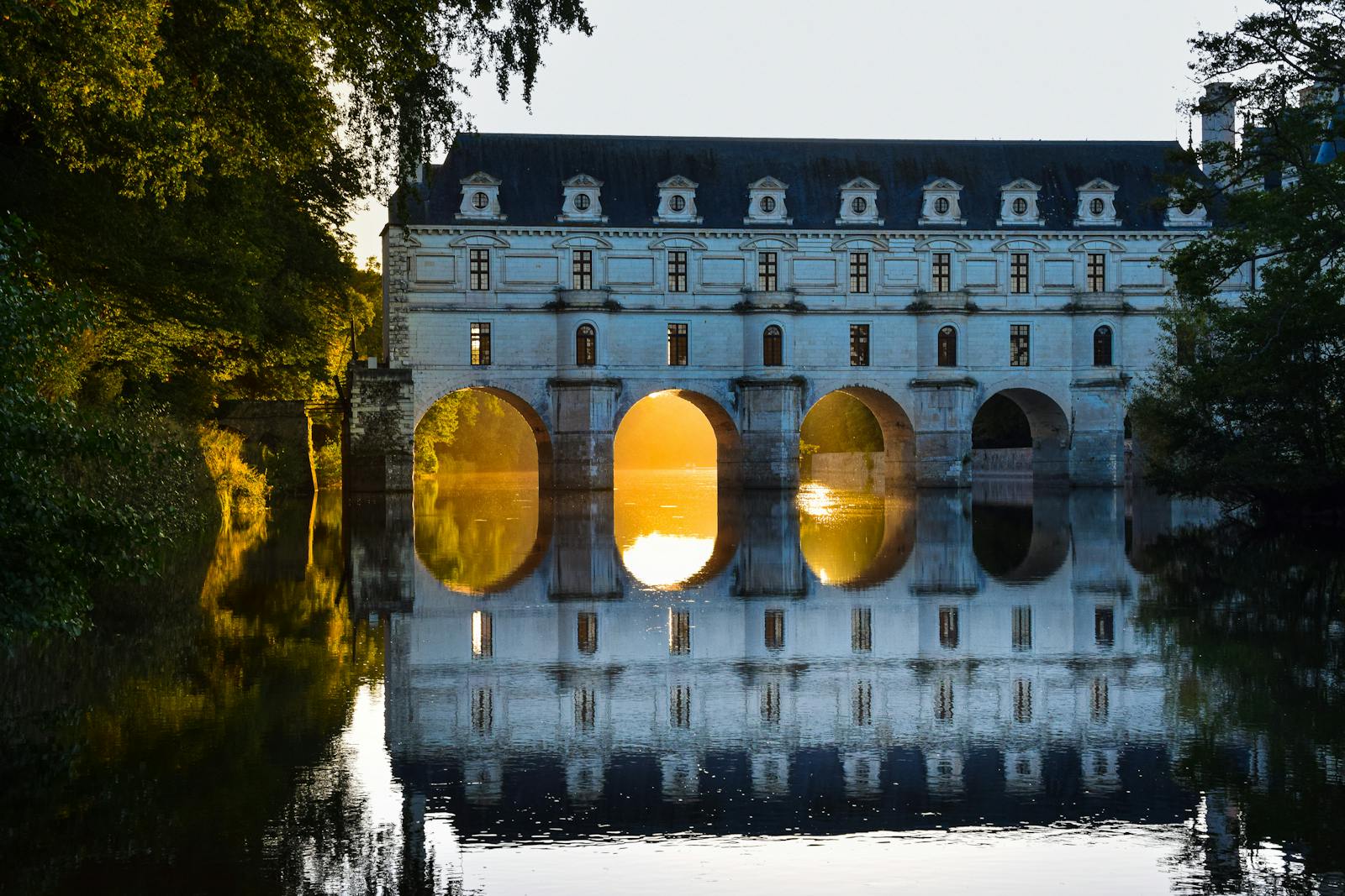 Château de Chenonceau beautifully reflected at sunset, highlighting its arches and elegant architecture.