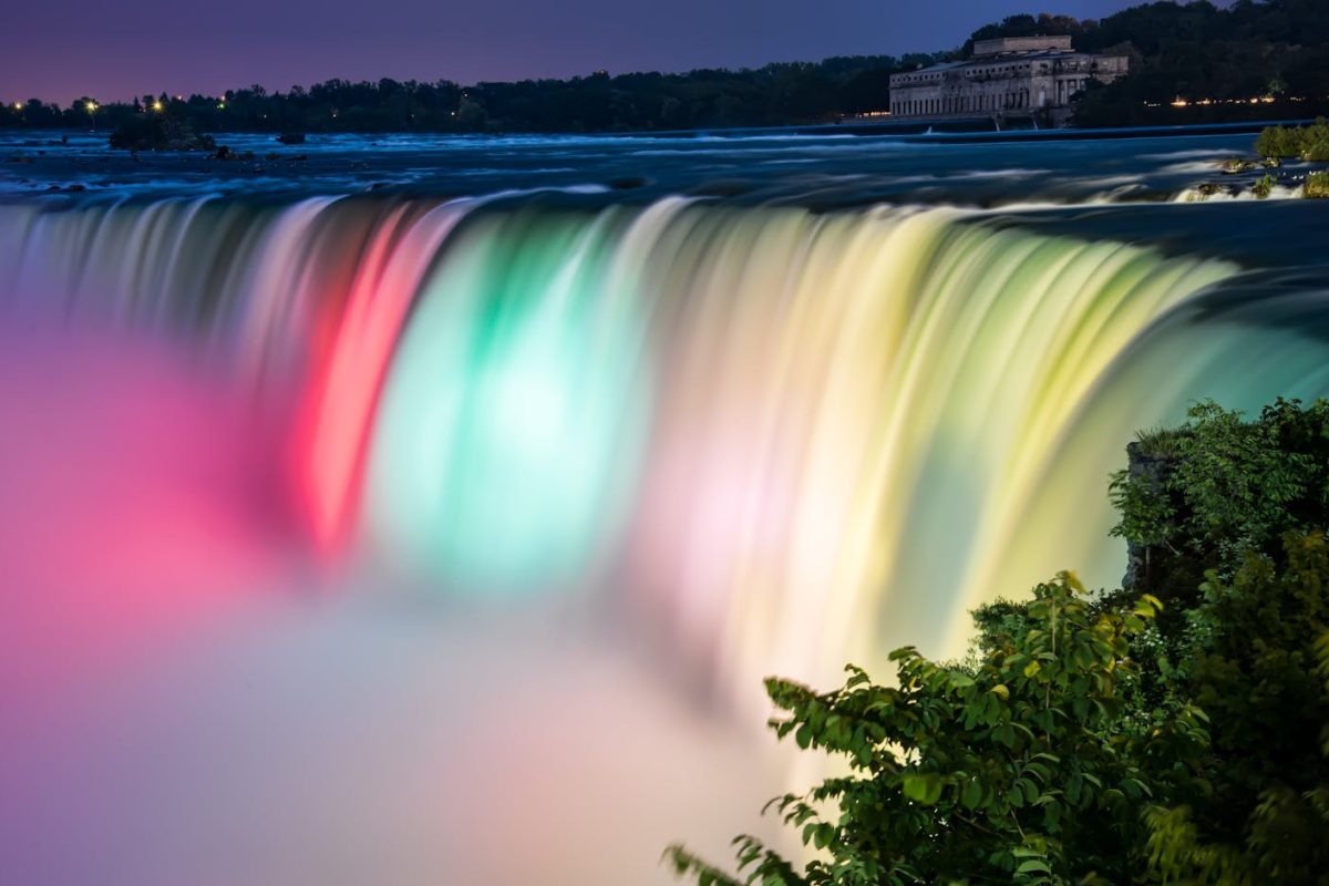 Stunning long exposure shot of Niagara Falls illuminated at night, showcasing colorful flowing water and mist.