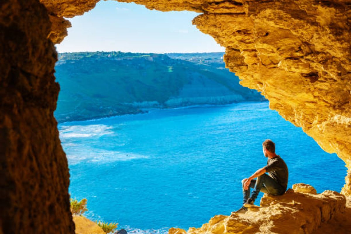 Gozo Island Malta, a young men and a View of Ramla Bay, from inside Tal Mixta Cave Gozo looking out over the blue ocean on a bright day during winter in Malta